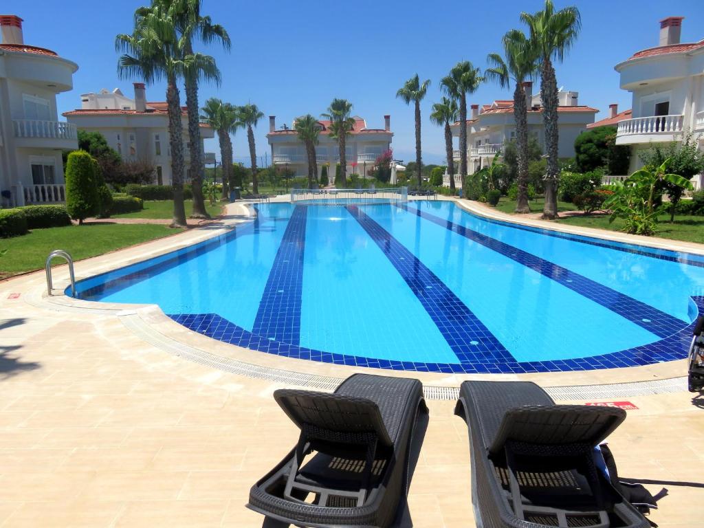 a swimming pool with two chairs and palm trees at TALYA TURİZM TATİLEVLERİ ve VİLLALARI in Belek