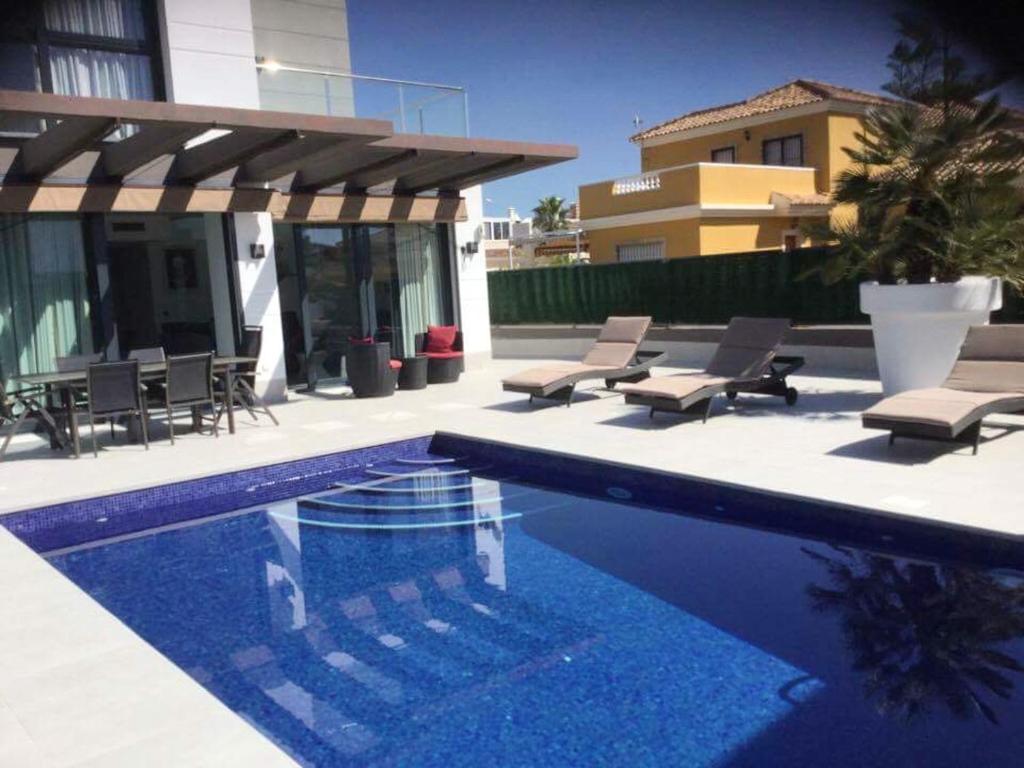 - une piscine avec des chaises et une maison dans l'établissement 3 bedrooms villa with lake view private pool and enclosed garden at Guardamar del Segura 2 km away from the beach, à Guardamar del Segura