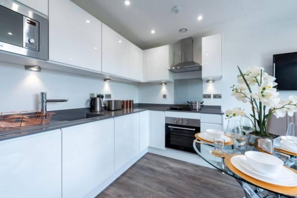 eine Küche mit weißen Schränken, einem Tisch und einem Waschbecken in der Unterkunft A beautiful brand new flat 25-minute to London in Luton