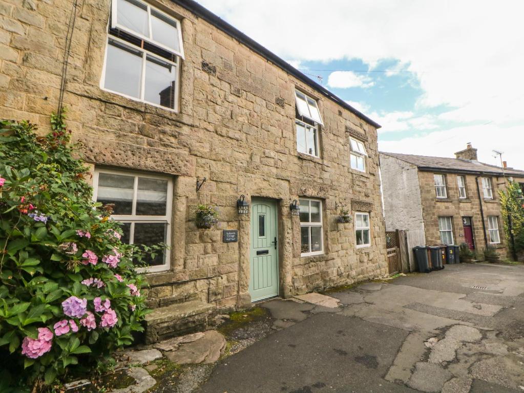 a brick building with a green door and flowers at Ardeevin Cottage in Buxton