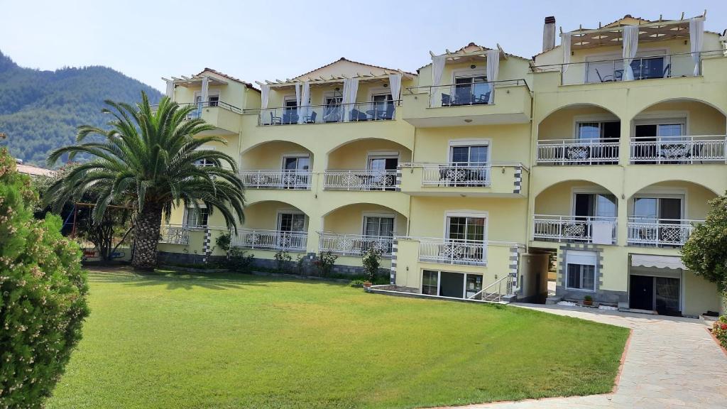 a large yellow building with a palm tree in front of it at Studios Rania in Skala Potamias