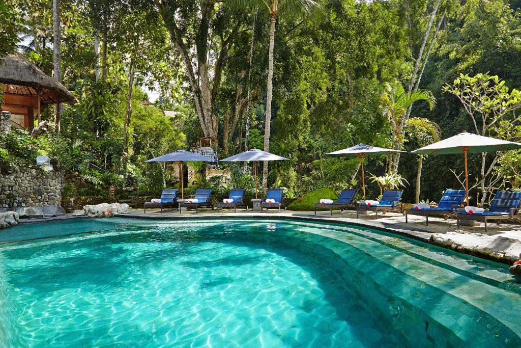 a swimming pool with blue chairs and umbrellas at Hotel Tjampuhan Spa in Ubud