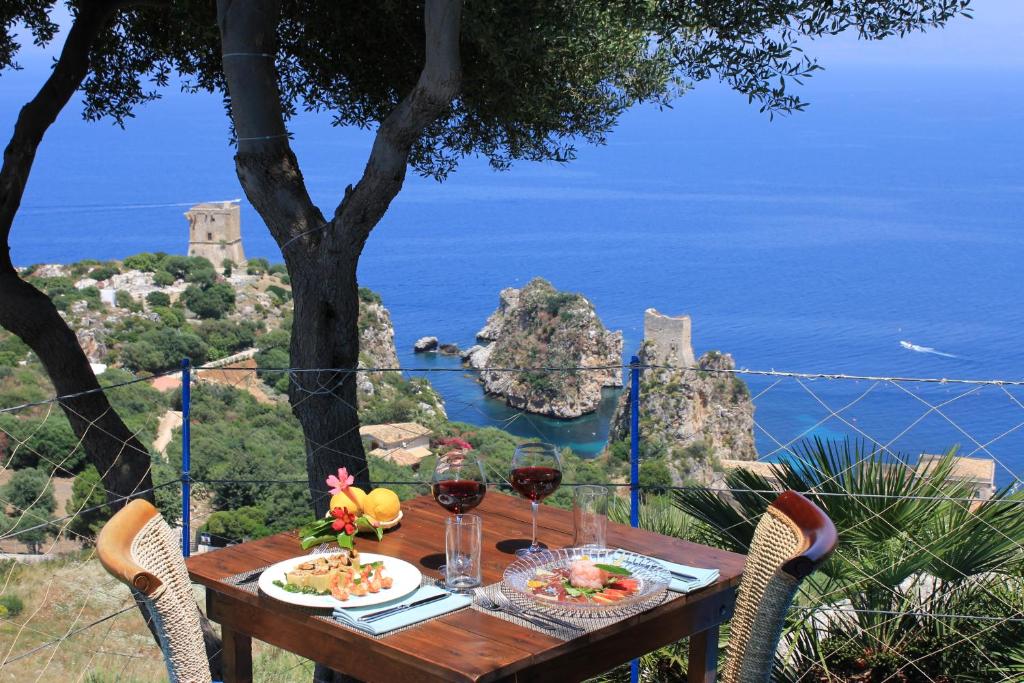 a wooden table with food and wine glasses on a view of the ocean at Torre Bennistra in Scopello