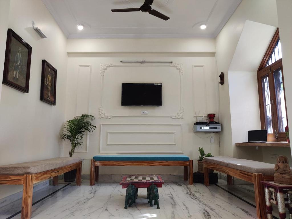 a living room with two benches and a flat screen tv at The Karauli Villa by Le Pension Stays in Jaipur