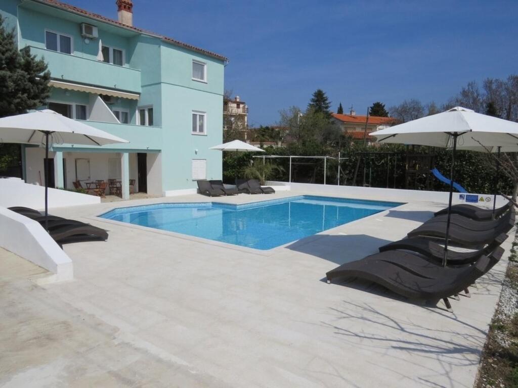 a swimming pool with chairs and umbrellas next to a house at Resindenz Benni 7 mit beheiztem grossem Pool in Medulin