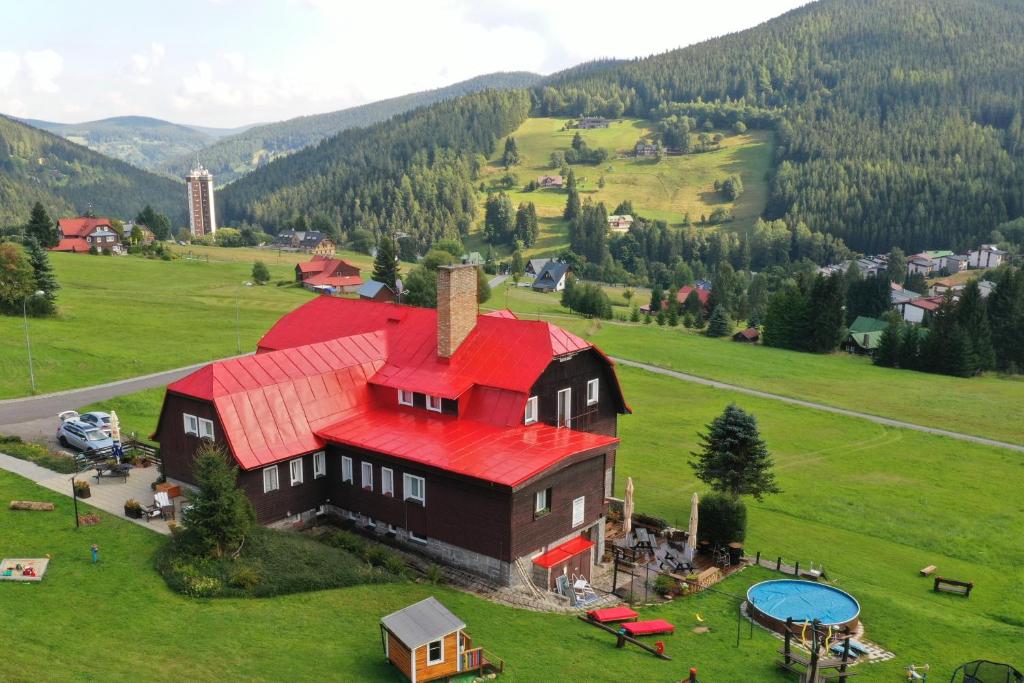 a large house with a red roof on a green field at Penzion Logla in Pec pod Sněžkou