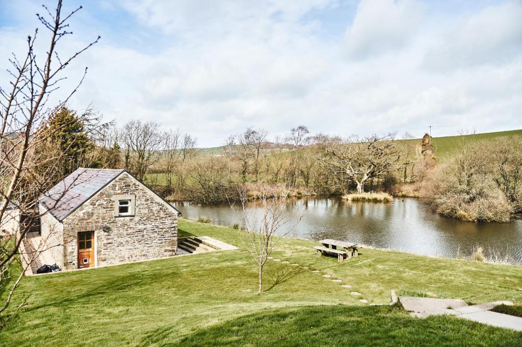 a stone house on a hill next to a lake at Penuwch Boathouse- Lakeside rural cottage ideal for families with indoor heated pool in Carmarthen