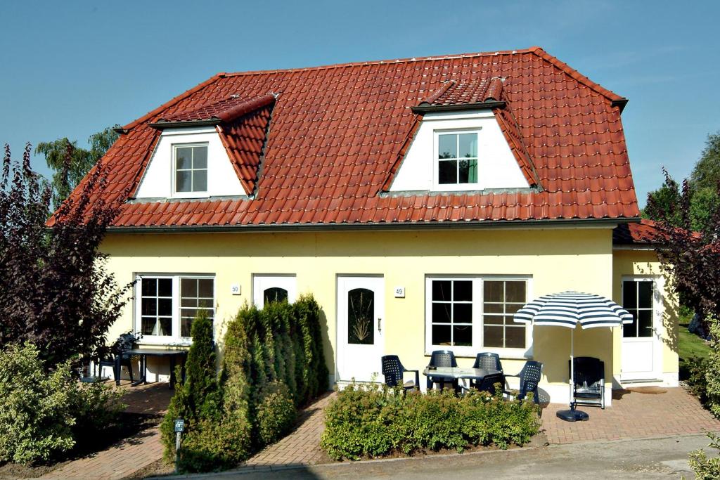 une maison blanche avec un toit rouge, des chaises et un parasol dans l'établissement Am Deich 47, à Zingst