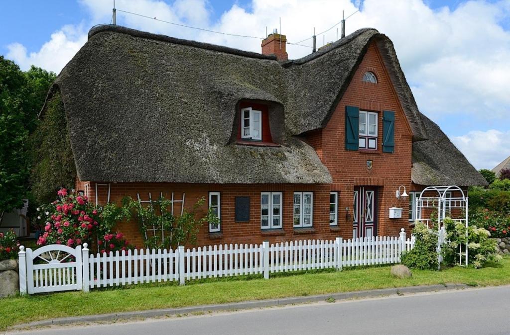 an old house with a thatched roof with a white fence at Ferien unterm Reetdach Whg 03 in Oevenum
