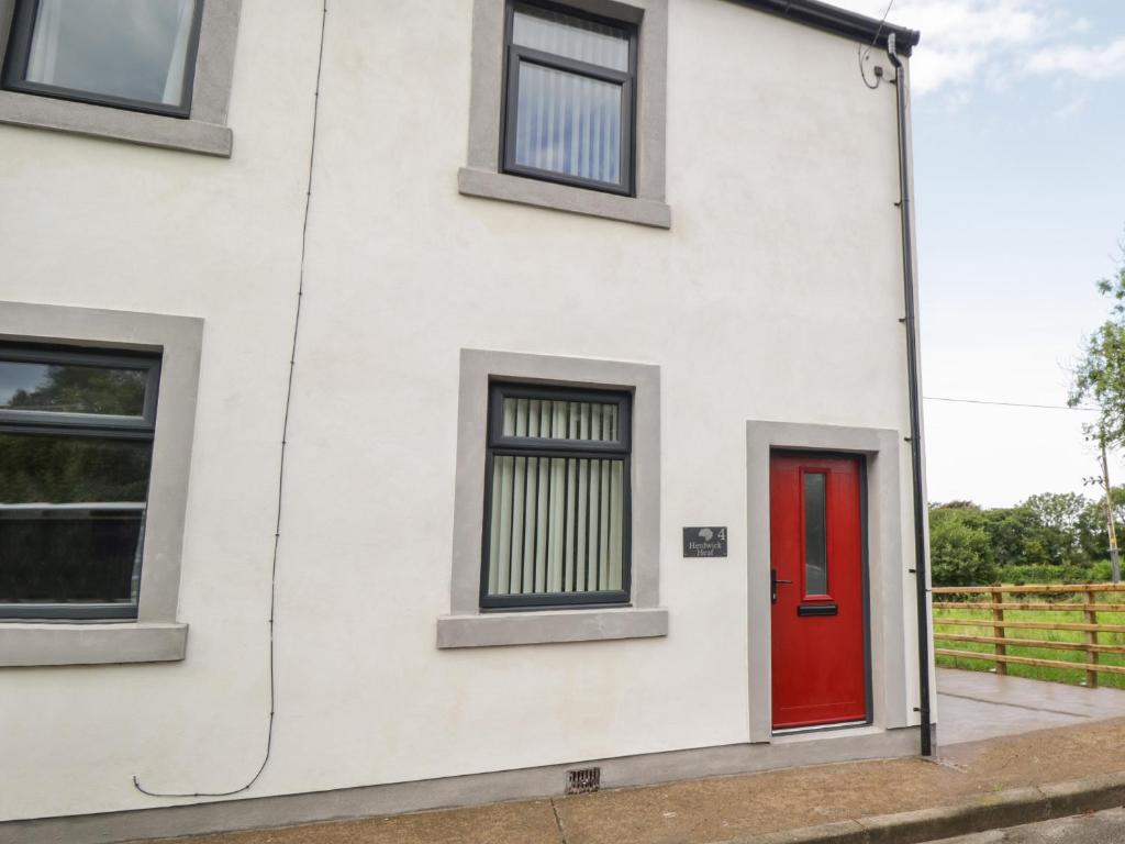 a white house with a red door and windows at Herdwick Heaf in Cleator