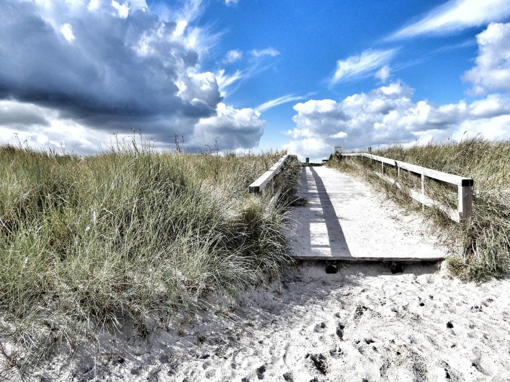 un puente de madera sobre una playa de arena con un cielo nublado en Ferienhaus-Engelking, en Dahme
