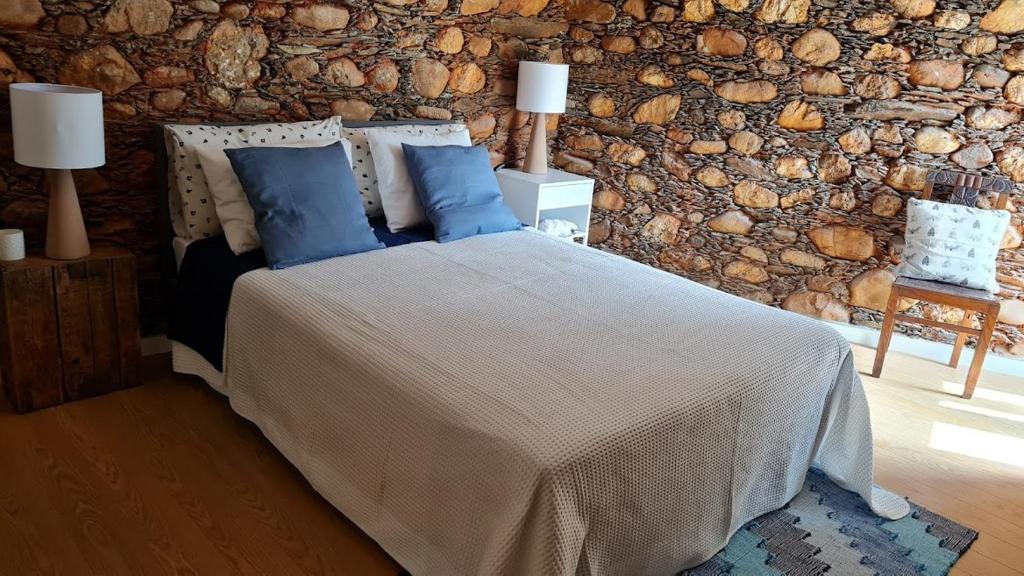 a bedroom with a bed with blue pillows and a stone wall at Casa da Ti Adélia in Janeiro de Cima