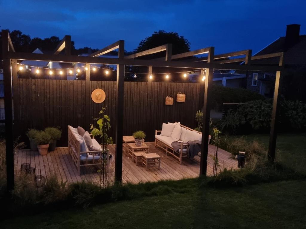 a wooden deck with chairs and a pergola with lights at Villa Grötvik in Halmstad