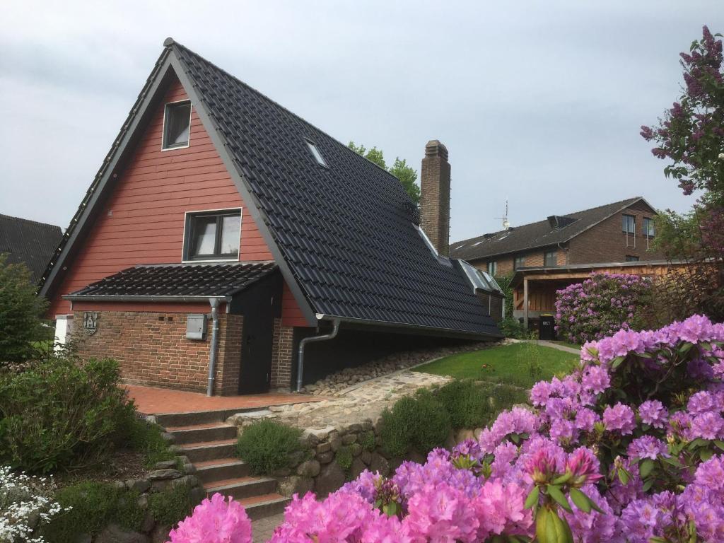 a red house with a black roof with pink flowers at Aukamp in Bünsdorf