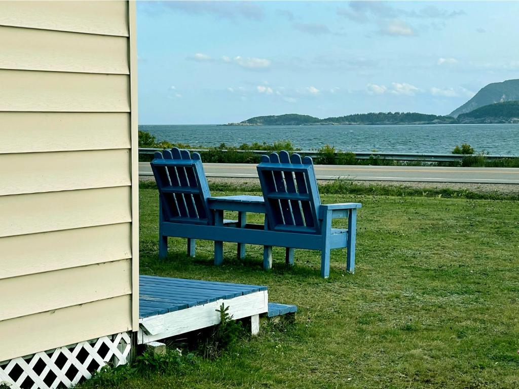 Deux chaises bleues assises dans l'herbe à côté d'une maison dans l'établissement Sea Breeze Motel, à Ingonish