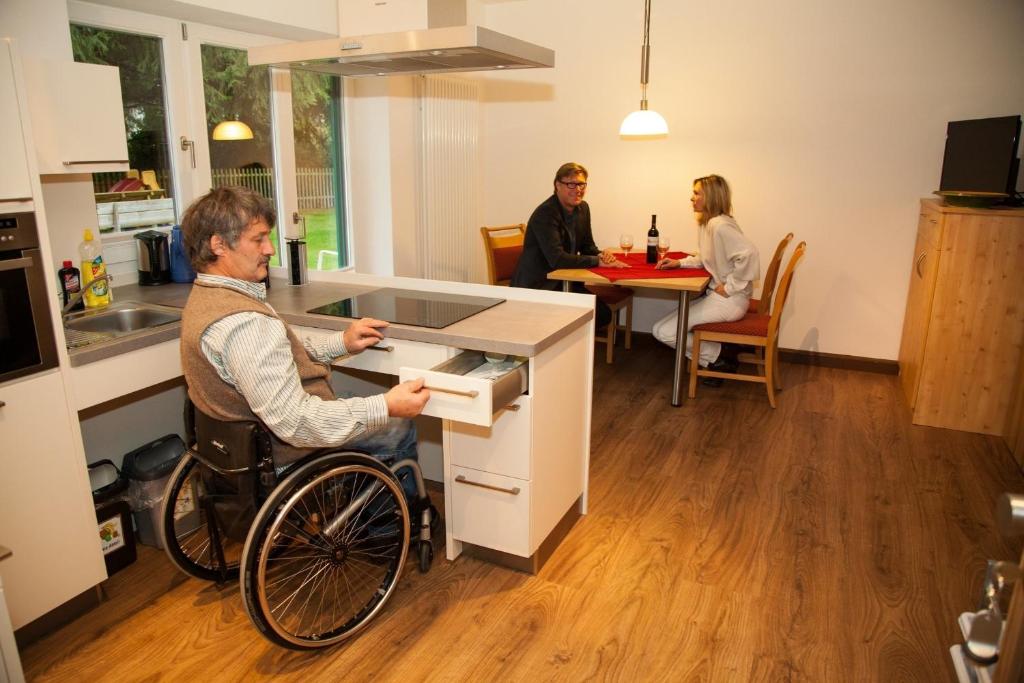 drie mensen in een keuken met een man in een rolstoel bij Koglkopf in Bad Wiessee