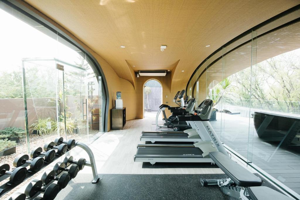 A long, bright fitness room has treadmills, benches, dumbbells, and curved glass walls.