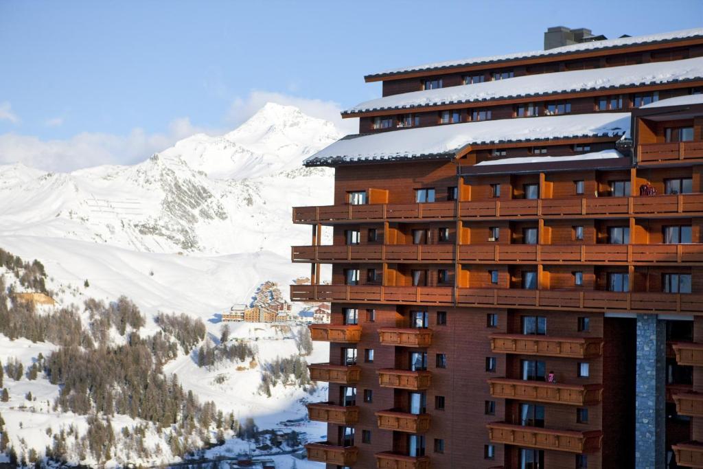 un edificio con una montaña cubierta de nieve en el fondo en travelski home premium - Résidence Les Hauts Bois 4 stars, en Aime La Plagne