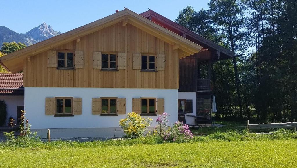 a house with a wooden roof and a grass field at Ferienwohnung Uferweg in Fischbachau