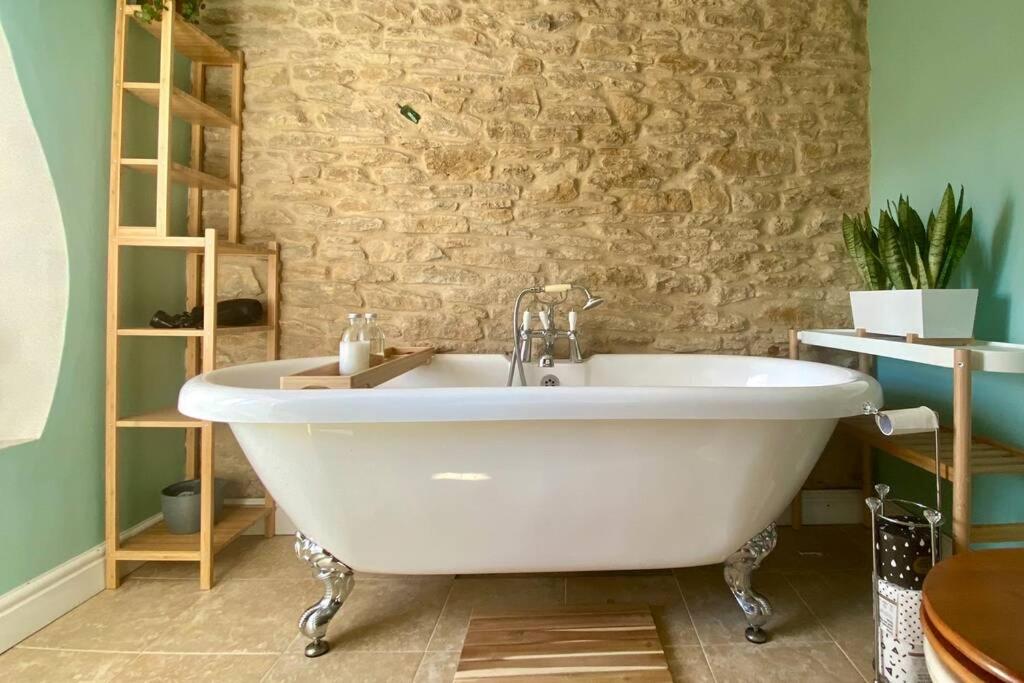 a white tub in a bathroom with a stone wall at The Explorers Rest - Cottage - Frome in Buckland Dinham