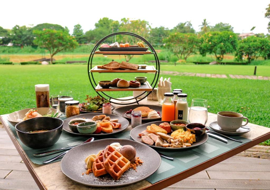 A generously styled breakfast spread is set on a terrace overlooking green grounds.