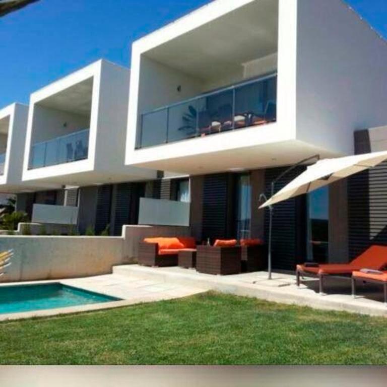 a large white house with a pool and an umbrella at Luxus Chalet Casas blancas in Cala Mendia