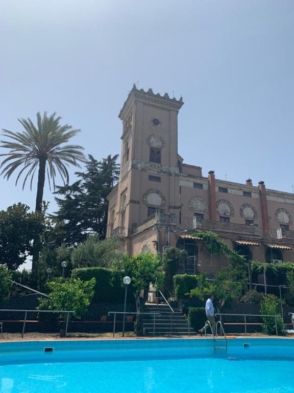 a building with a clock tower behind a swimming pool at Villa con piscina in Mascalucia