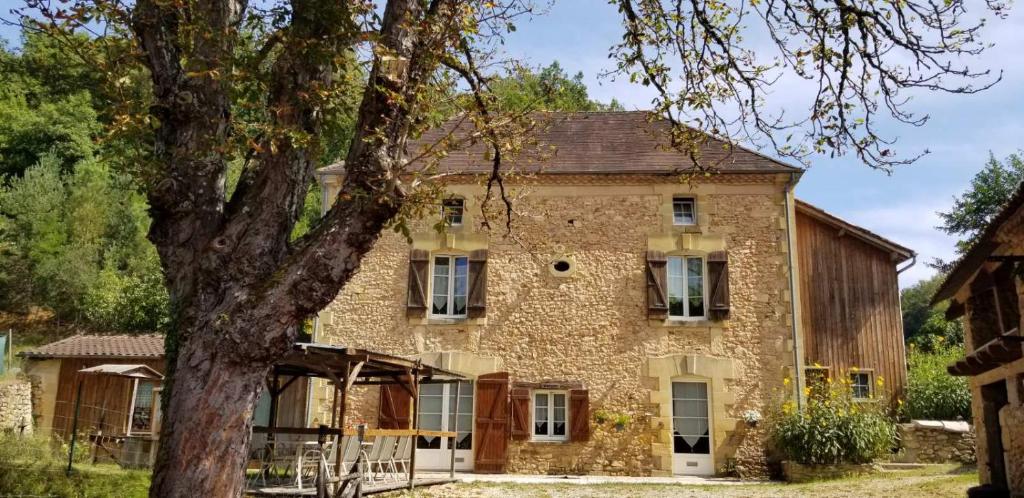 une vieille maison en pierre avec un arbre en face de celle-ci dans l'établissement Moulin de l'Hoste, à Larzac