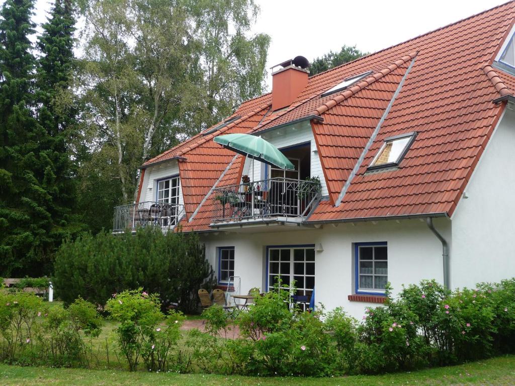 a white house with an orange roof and a balcony with an umbrella at FeWo Abendsonne in Prerow