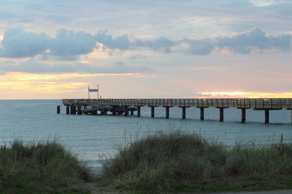 a pier in the ocean with the sun setting at Muschelkoje in Stakendorfer Strand