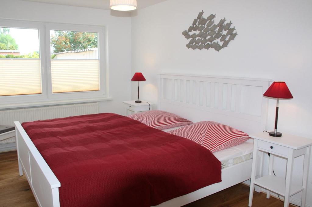a white bedroom with a red bed and two windows at Feldlerche in Neue Tiefe Fehmarn