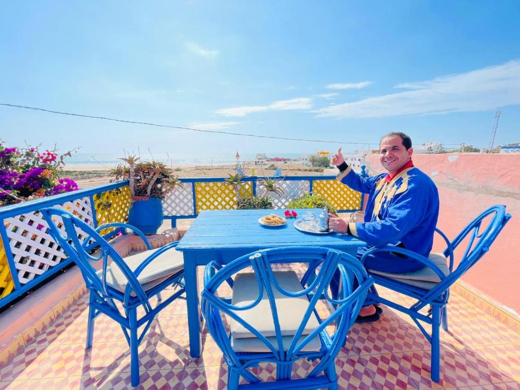 Ein Mann, der an einem blauen Tisch auf einem Balkon sitzt. in der Unterkunft dar boujdaa in Sidi Kaouki