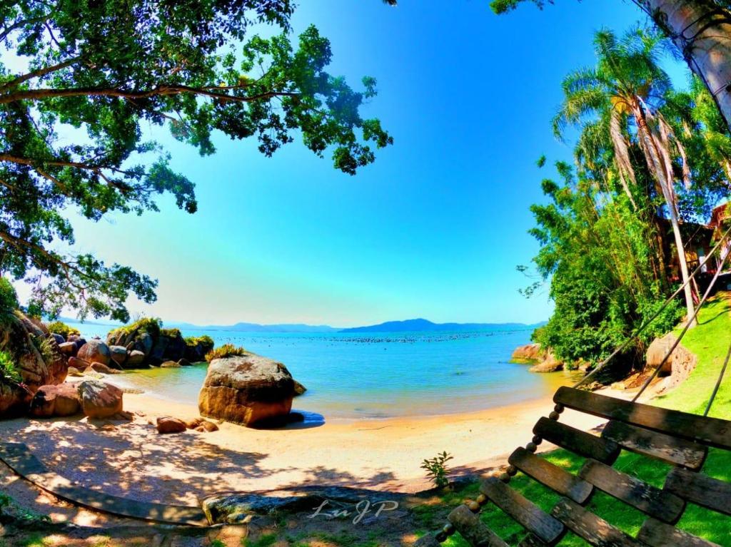 een strand met een bank en water en bomen bij Villa dos Ganchos in Governador Celso Ramos