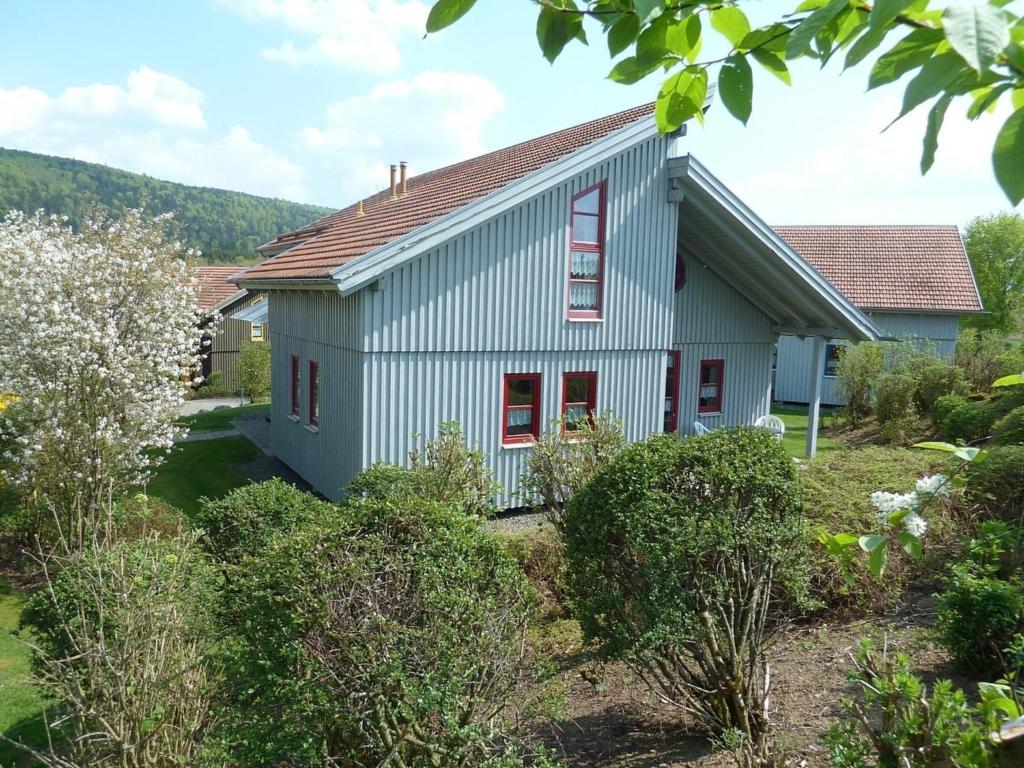 une maison blanche avec des fenêtres rouges dans une cour dans l'établissement Ferienhaus Nr 10A2, Feriendorf Hagbügerl, Bayr Wald, à Waldmünchen