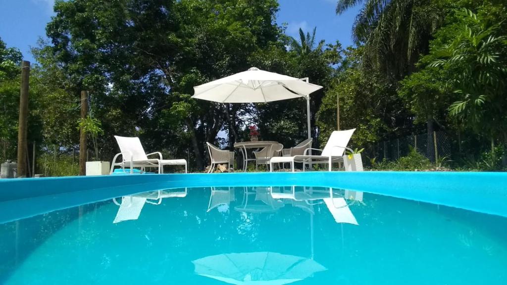 einen Pool mit einem Tisch, Stühlen und einem Sonnenschirm in der Unterkunft RECANTO DE ZEZE in Ilhéus