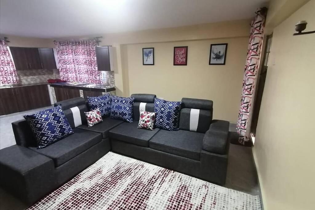ein Wohnzimmer mit einem schwarzen Sofa und Kissen in der Unterkunft Lass Grove Home in Kisii