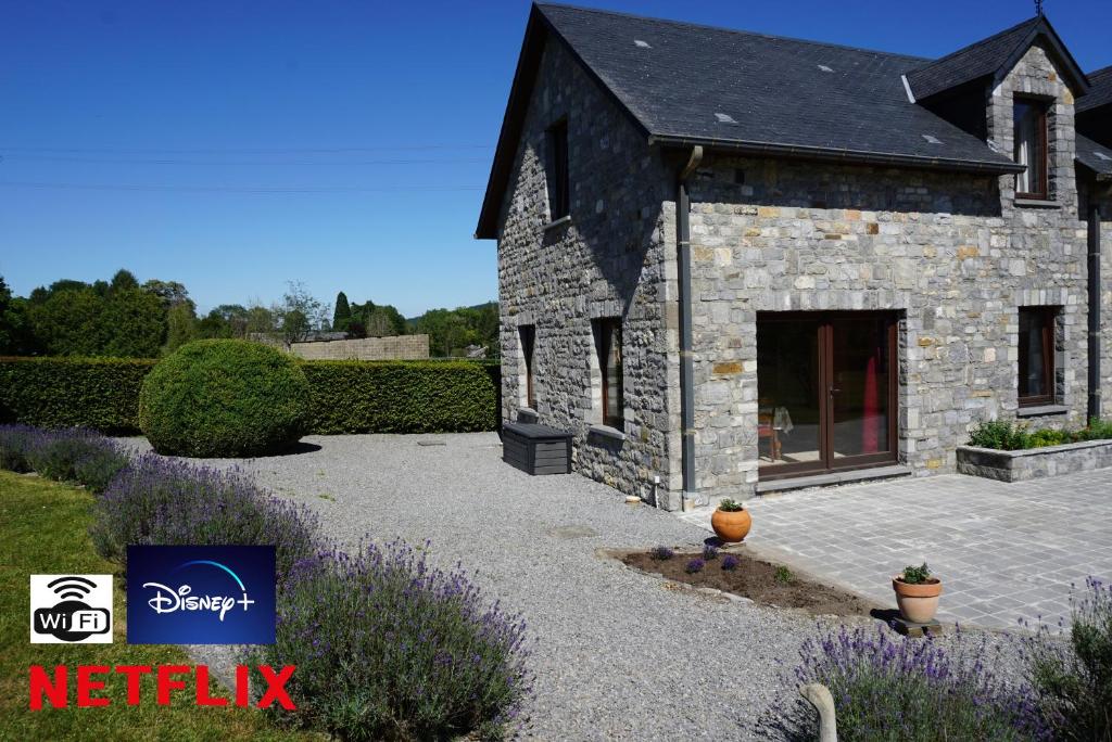 una casa de piedra con un patio con flores púrpuras en Gîte du Vieux Chemin en Durbuy