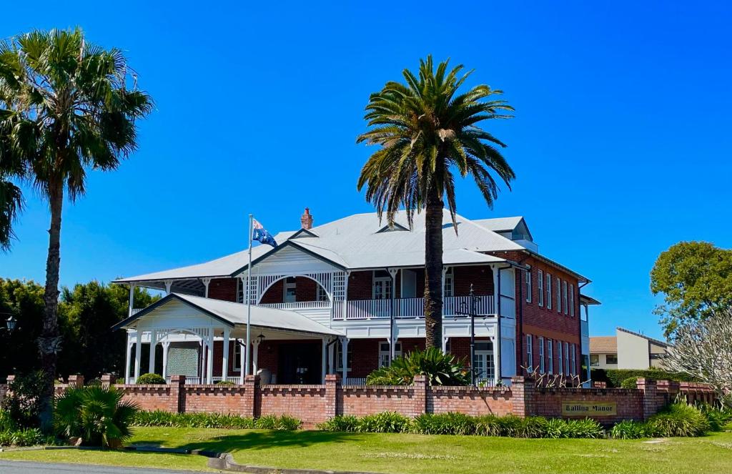 a large house with a palm tree in front of it at Ballina Manor Boutique Hotel in Ballina