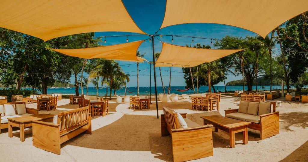 una playa con mesas, sillas y sombrillas en Café de Playa Beach Front Hotel en Coco