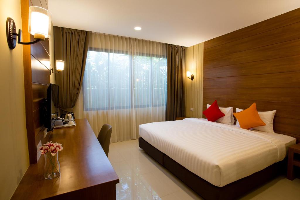 A bright double room pairs a large bed with a long wooden desk and a curtained window.