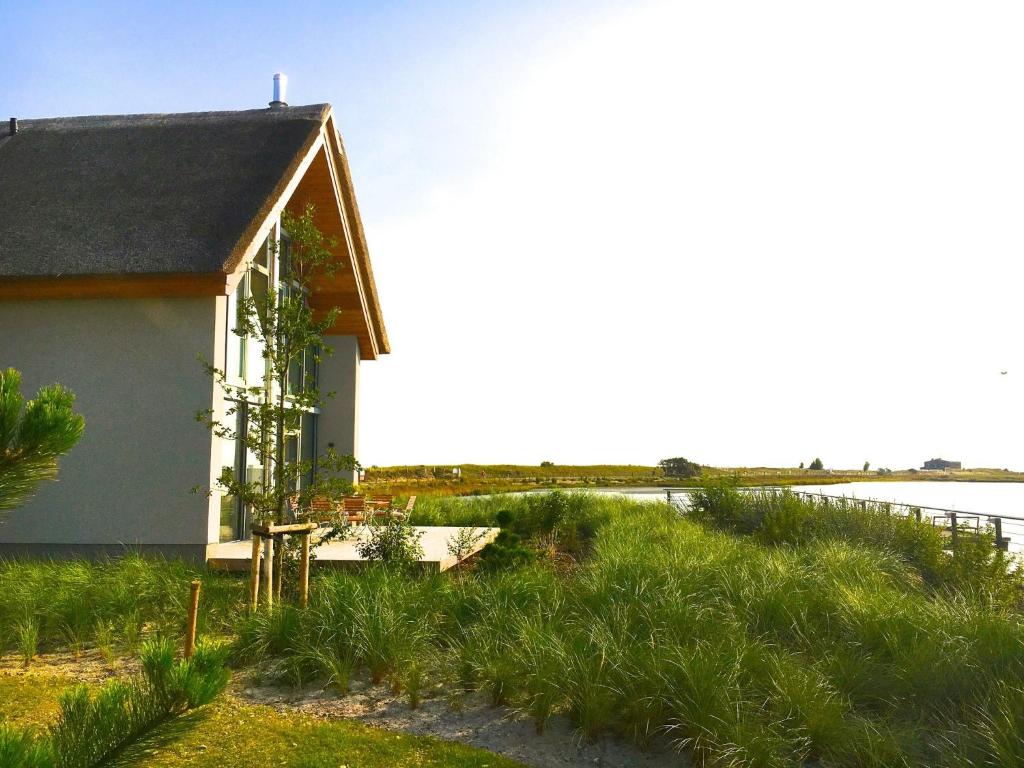 a house in the grass next to a body of water at Ostsee - Reetdachhaus Nr 46 "Strandrausch" im Strand Resort in Heiligenhafen