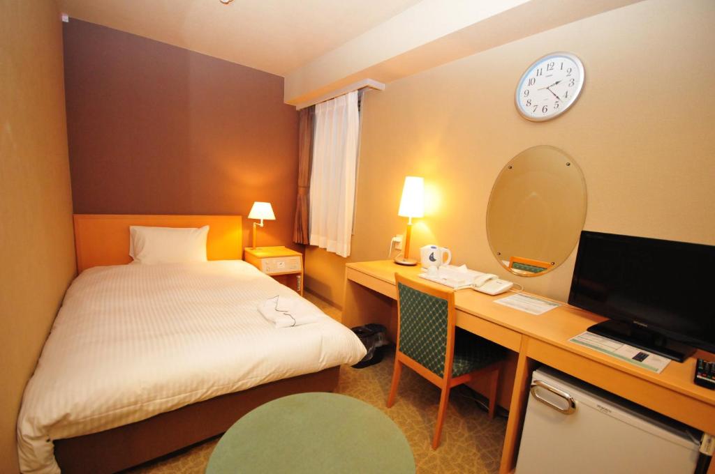 a hotel room with a bed and a desk and a clock at Hotel Premium Green Hills in Sendai