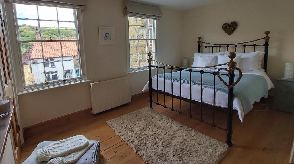 a bedroom with a bed and two windows at Dunsley Cottage in Staithes
