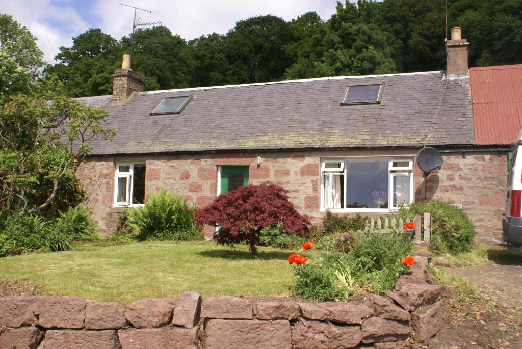 an old brick house with a stone wall and flowers at Smithy Cottage in Blairgowrie