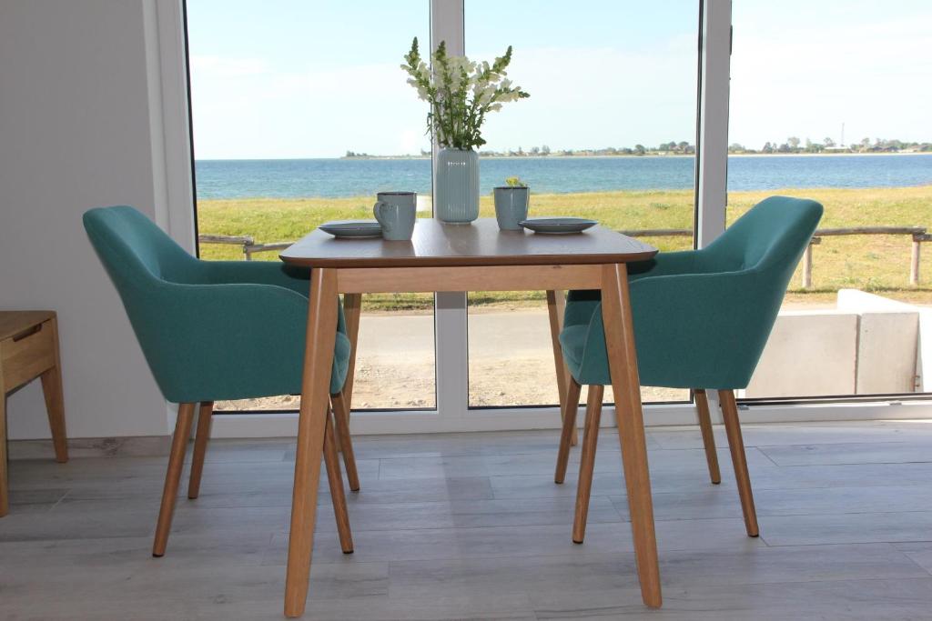 stół z 2 zielonymi krzesłami i stół z widokiem na ocean w obiekcie Meerblick Fehmarnsund 2 - direkt am Strand w mieście Fehmarnsund