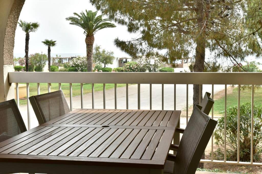 une table et des chaises en bois sur un balcon avec des palmiers dans l'établissement Le Byblos 7, à Argelès-sur-Mer