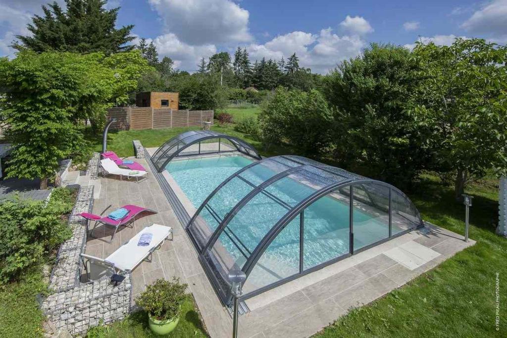 een zwembad met een glazen kas eromheen bij Au Coeur Du Bien Etre, chambre d'hôtes avec piscine chauffée et couverte, SPA, sauna, massages in Monteaux