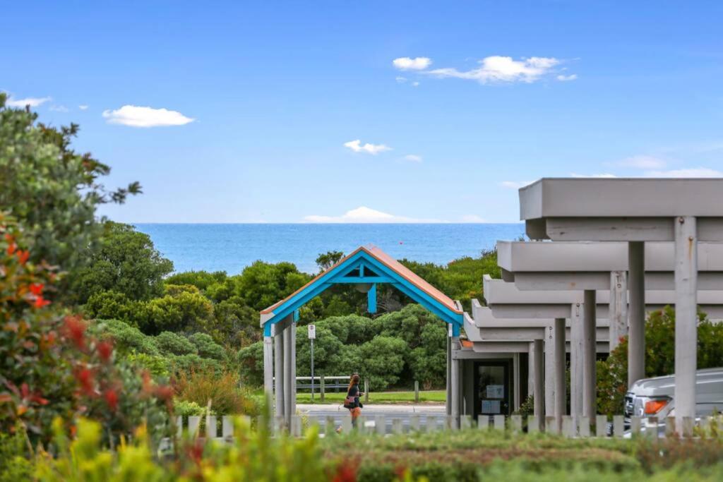 a person walking past a building with the ocean in the background at The Bay Beach Studio ~ Ocean View in Apollo Bay