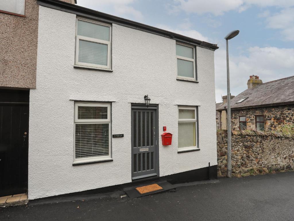 a white house with a red door on a street at Clydfan in Caernarfon