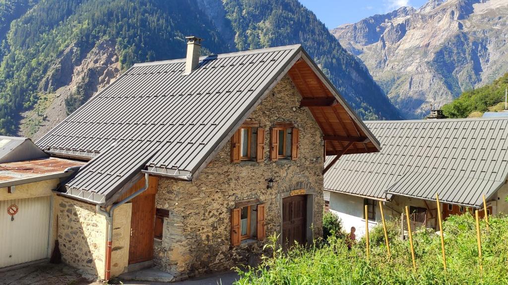 une maison en pierre avec un toit avec des montagnes en arrière-plan dans l'établissement La Grange St. Cyprien, Venosc - Les Deux Alpes, à Vénosc